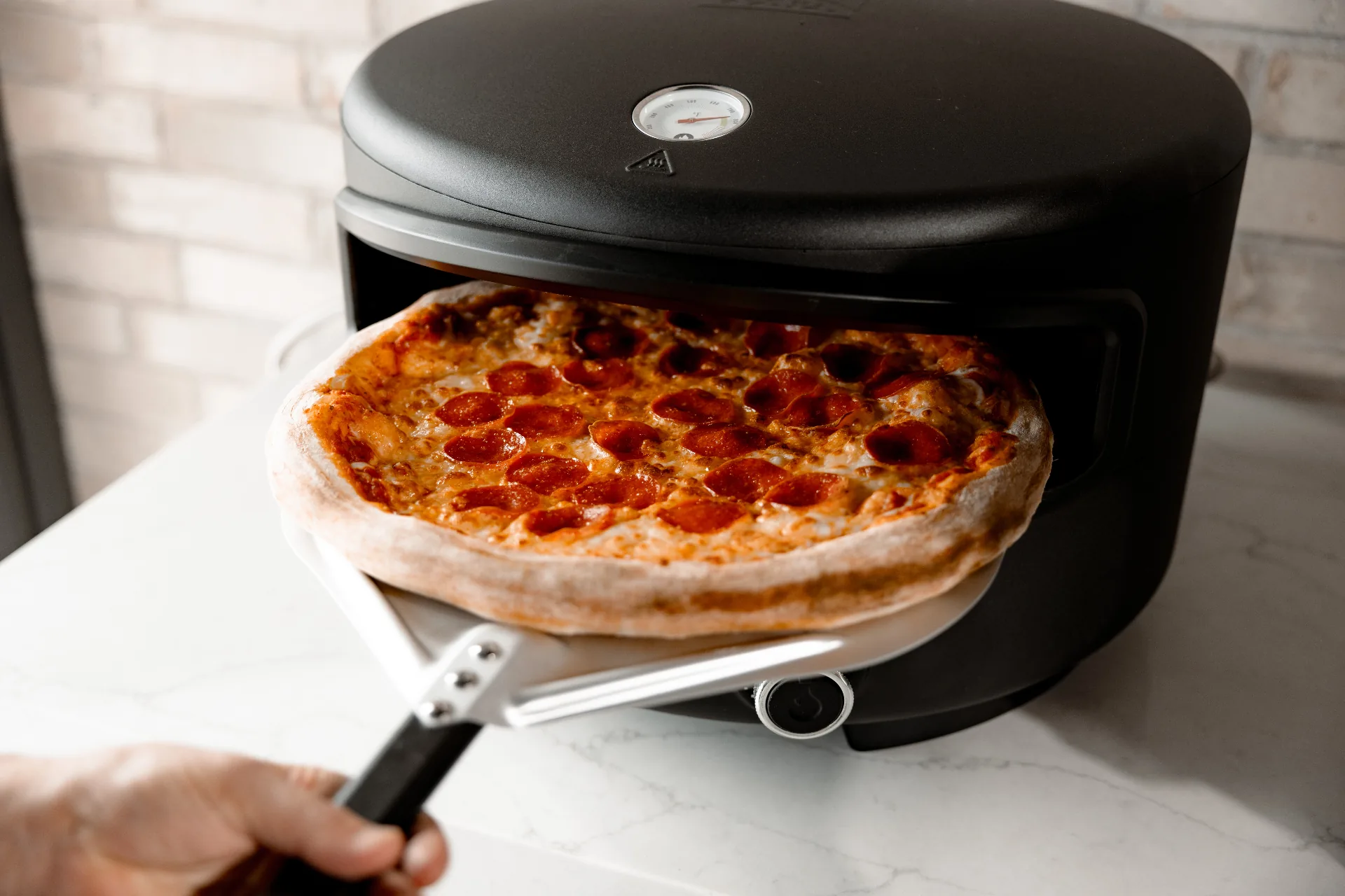 Host pulling perfect pizza from oven with guests watching